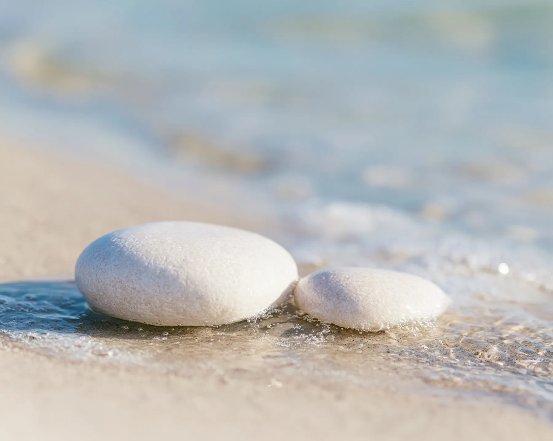 Zwei helle Kieselsteine, umspült von einer flachen Welle am Strand