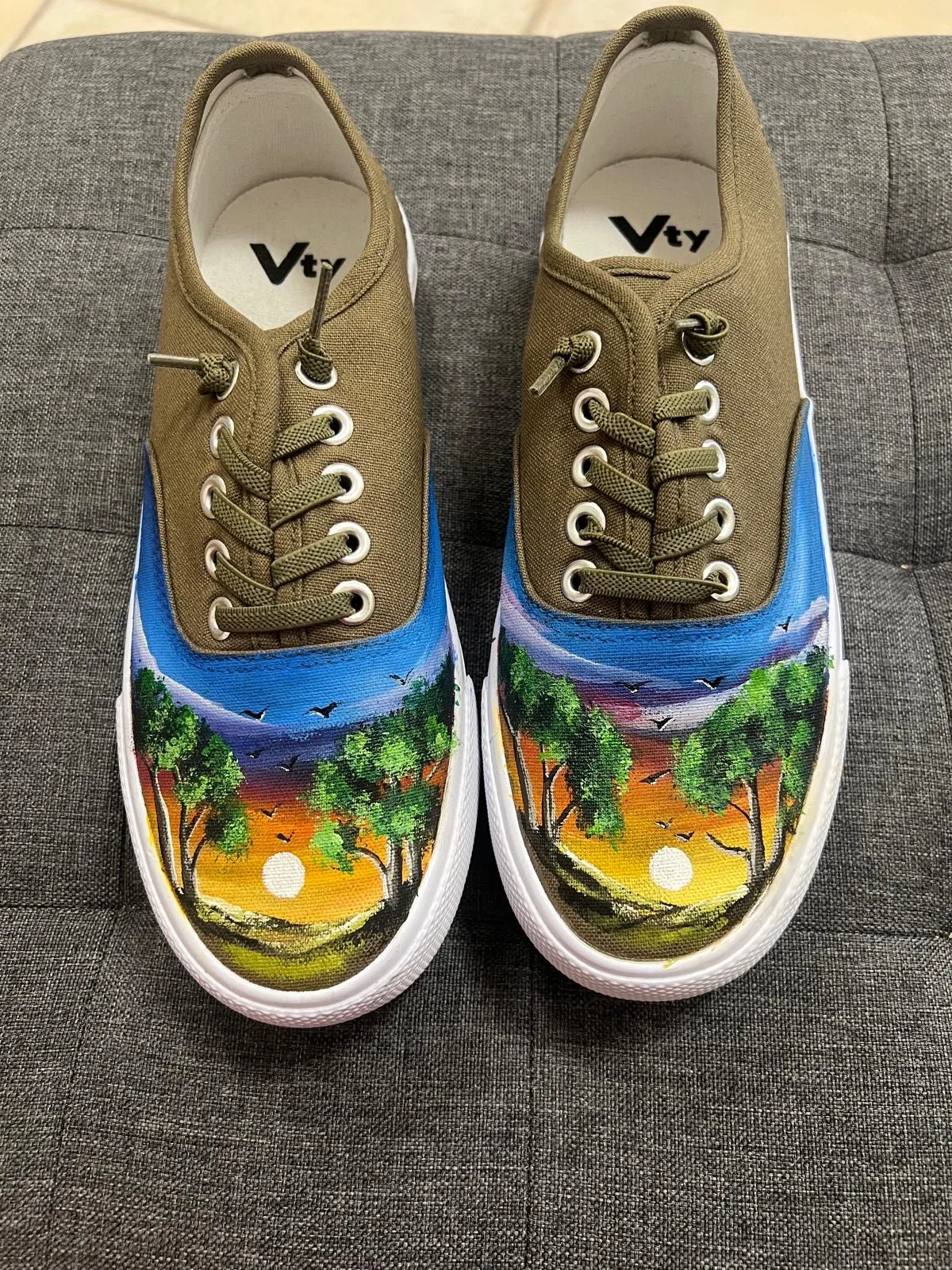 Olivgrüne Sneaker mit gemalter Abendsonne über einem See und Vogelschwarm